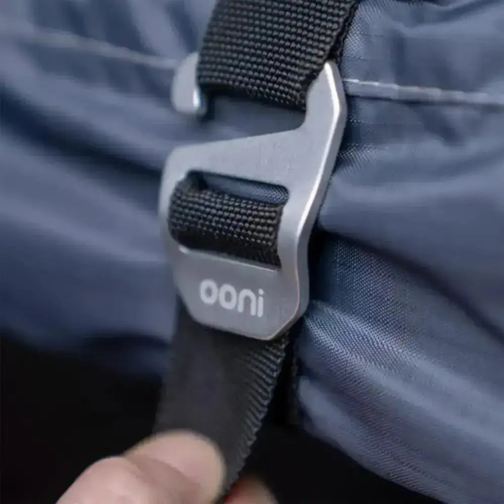 Close-up of a black strap with a silver buckle on a blue fabric background, featuring the 'ooni' brand.