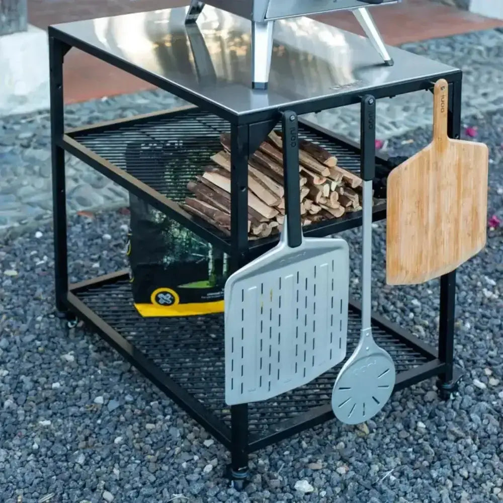 Outdoor grill with firewood, spatula, and wooden paddle on a stone surface