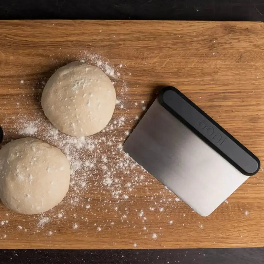 Two balls of dough on a wooden surface with a scraper next to them.