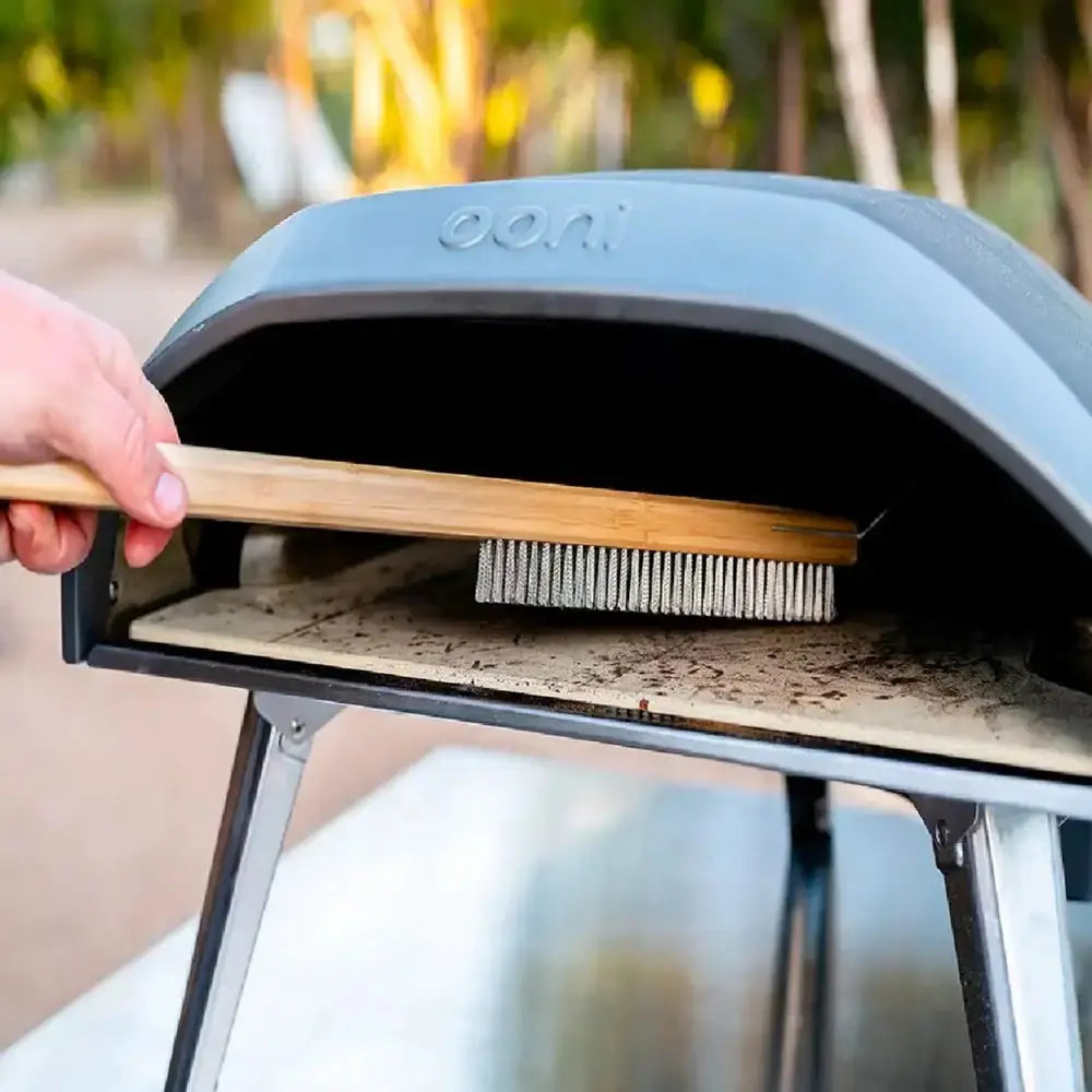 Person cleaning a portable pizza oven with a brush