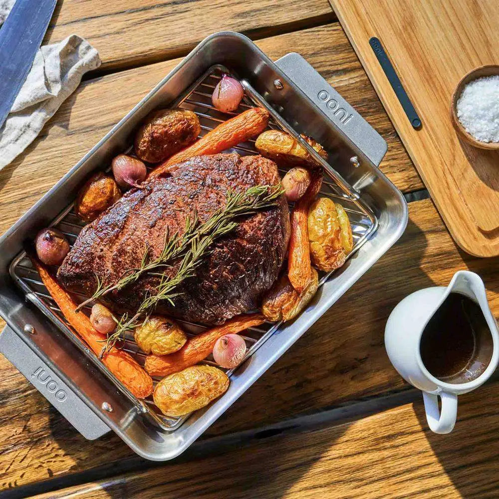 Roasted meat with vegetables in a roasting pan on a wooden table with a cup of coffee.