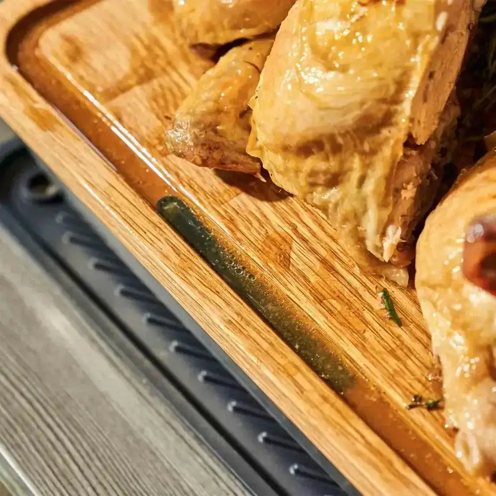 Wooden cutting board with roasted chicken pieces on a metal surface