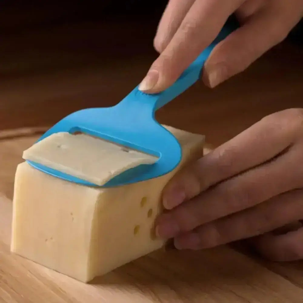 Person using a blue cheese slicer to cut a block of cheese on a wooden surface
