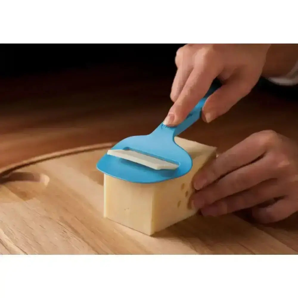 Person using a blue cheese slicer on a block of cheese on a wooden cutting board.