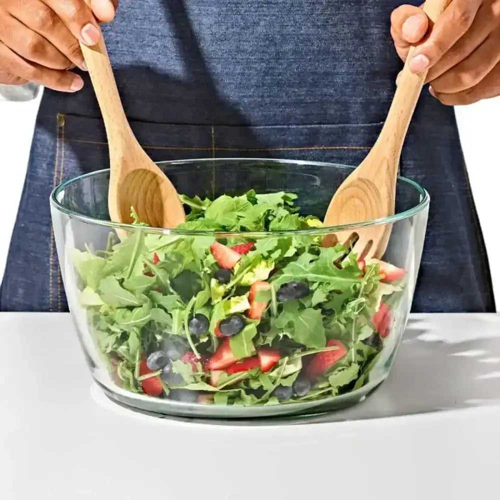 Oxo beechwood salad server set with clear glass bowl filled with fresh greens strawberries and blueberries
