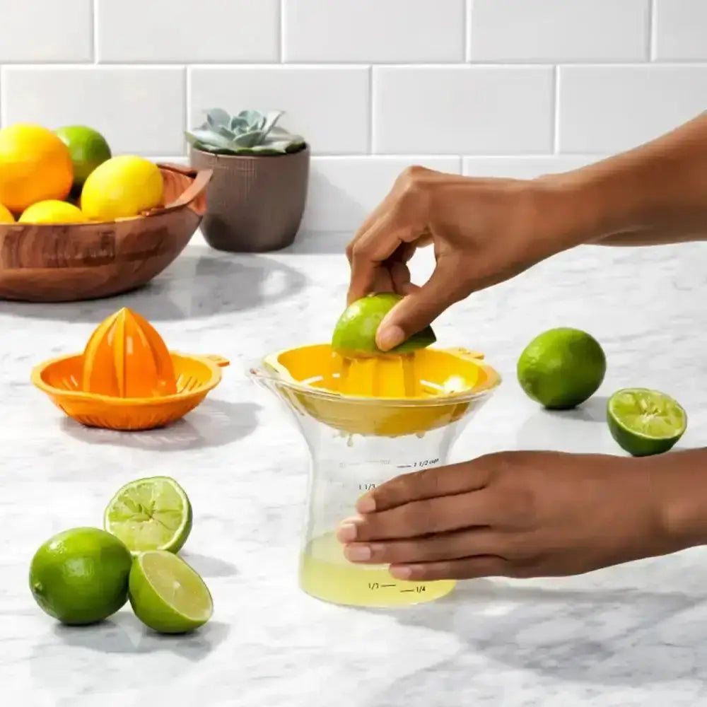 Person using a yellow manual juicer to extract juice from limes on a kitchen counter.