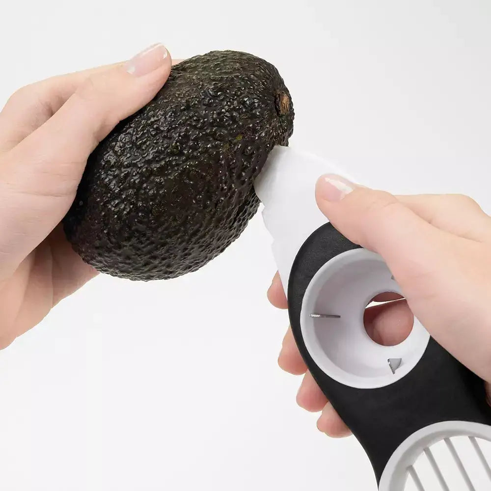 Hands using the avocado slicer to cut open an avocado