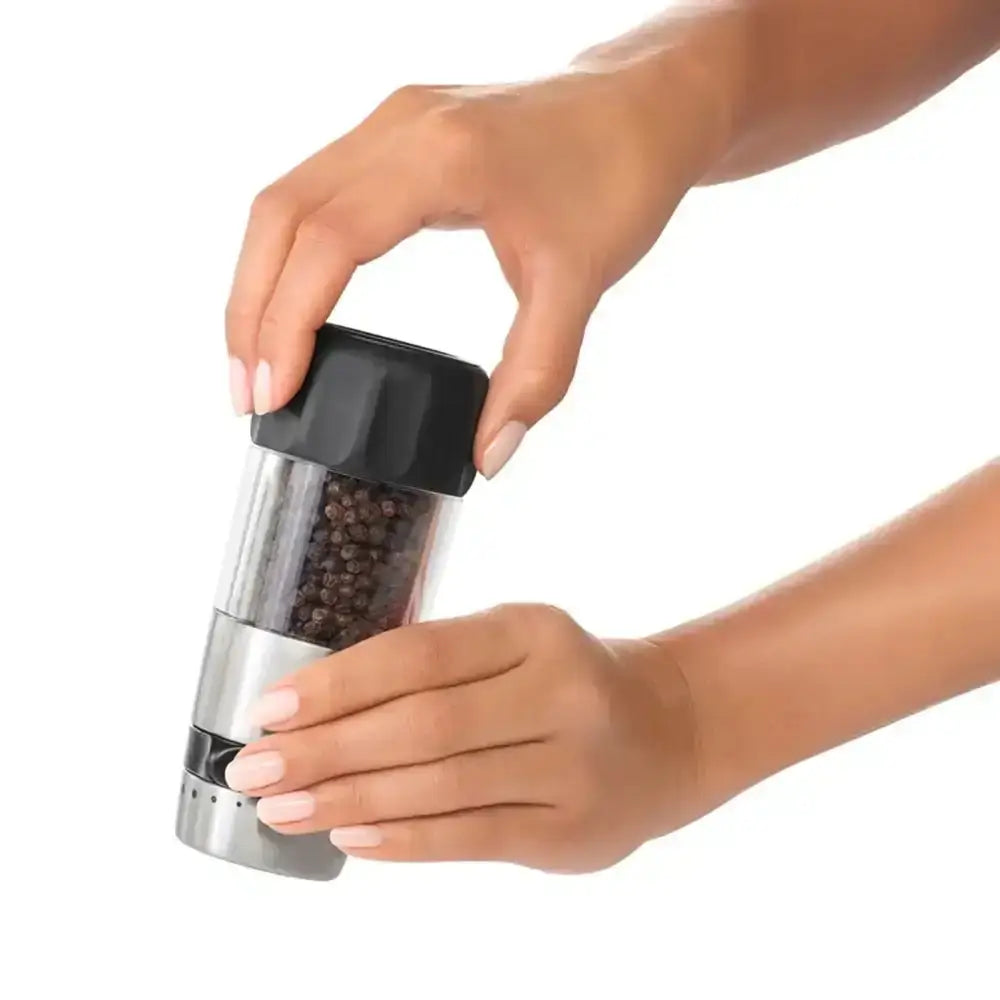 Hand holding a pepper grinder with black top and silver body on a white background