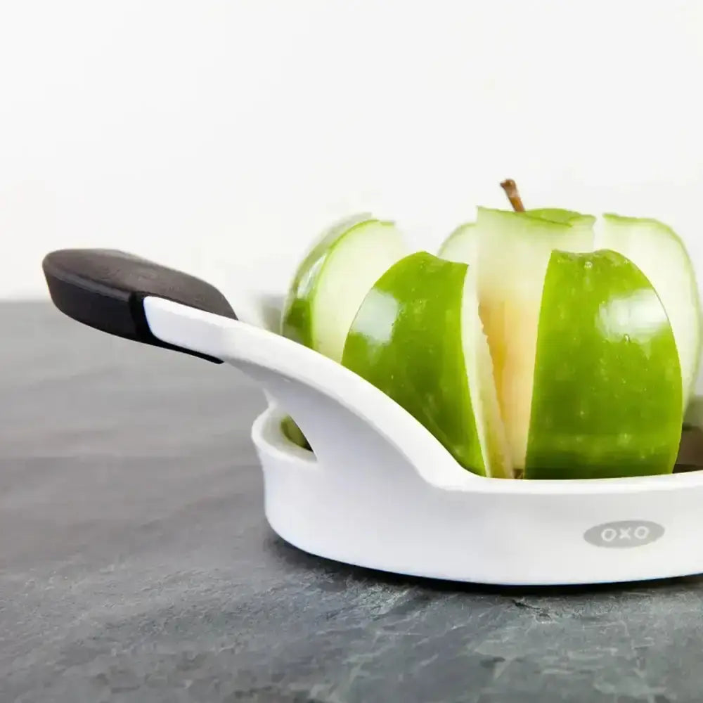 Green apple sliced with a white OXO apple slicer on a gray surface