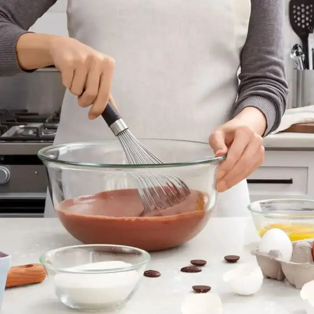 Person whisking chocolate mixture in a bowl with kitchen utensils and ingredients on the counter.