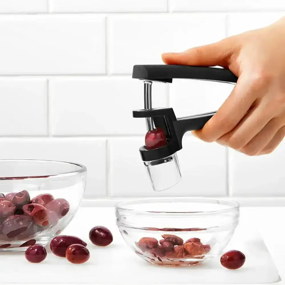 Hand using a cherry pitter to remove pits from cherries on a white surface.