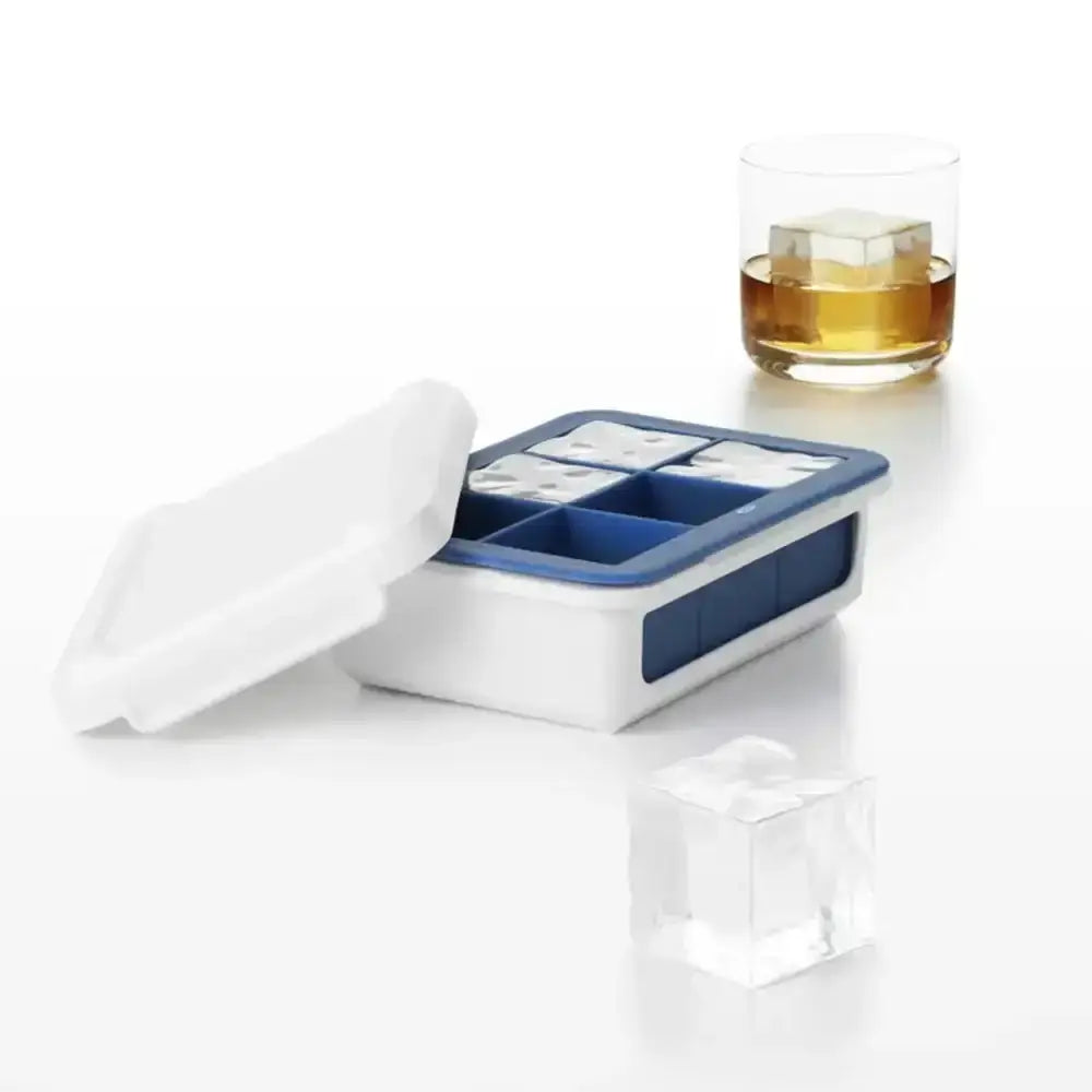Ice cube tray with blue compartments on a white surface, next to a glass of whiskey.