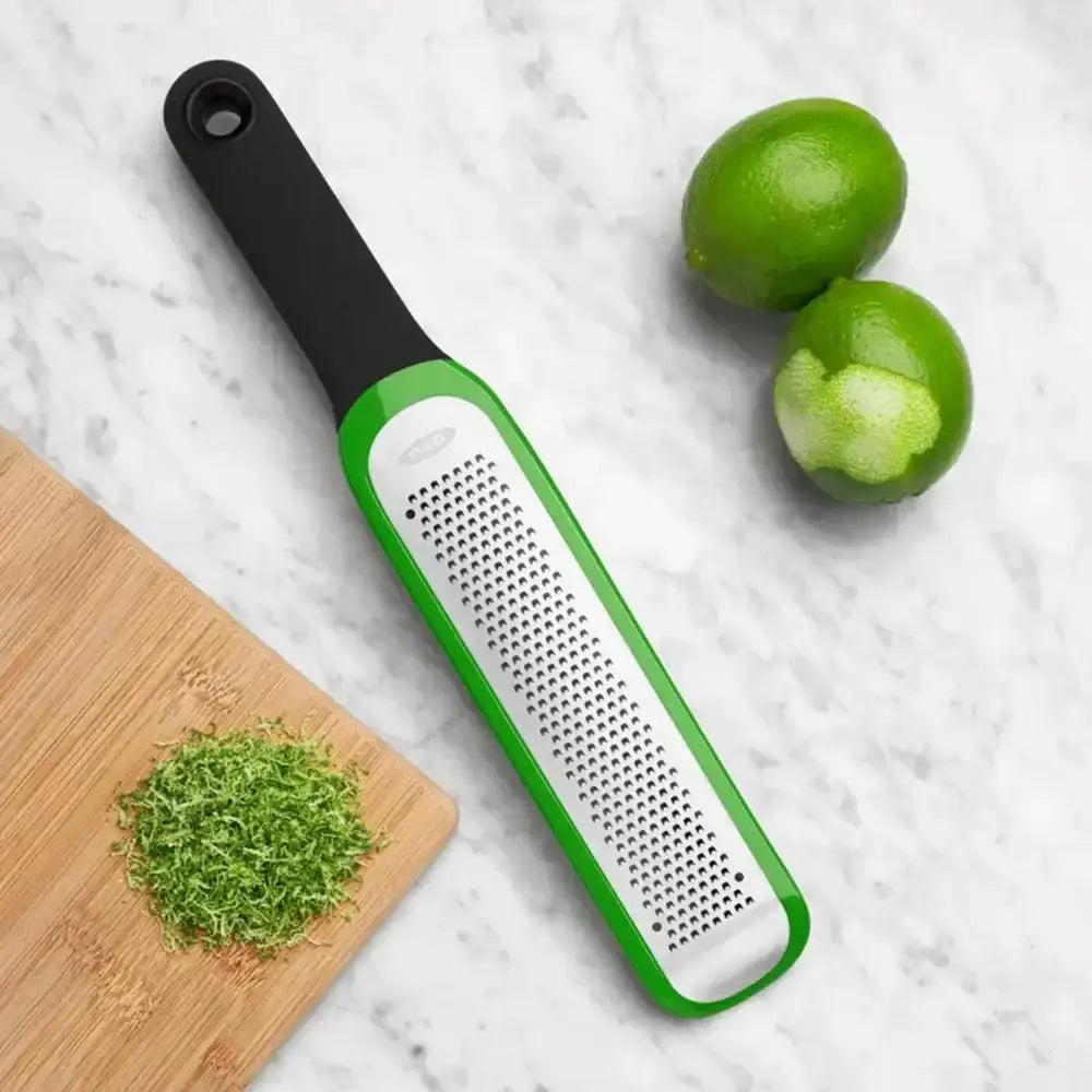 Green and white citrus reamer with limes and a wooden cutting board on a marble surface