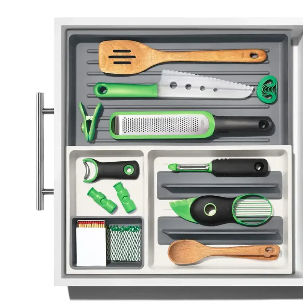 Set of kitchen utensils and tools organized in a drawer with green and black handles.