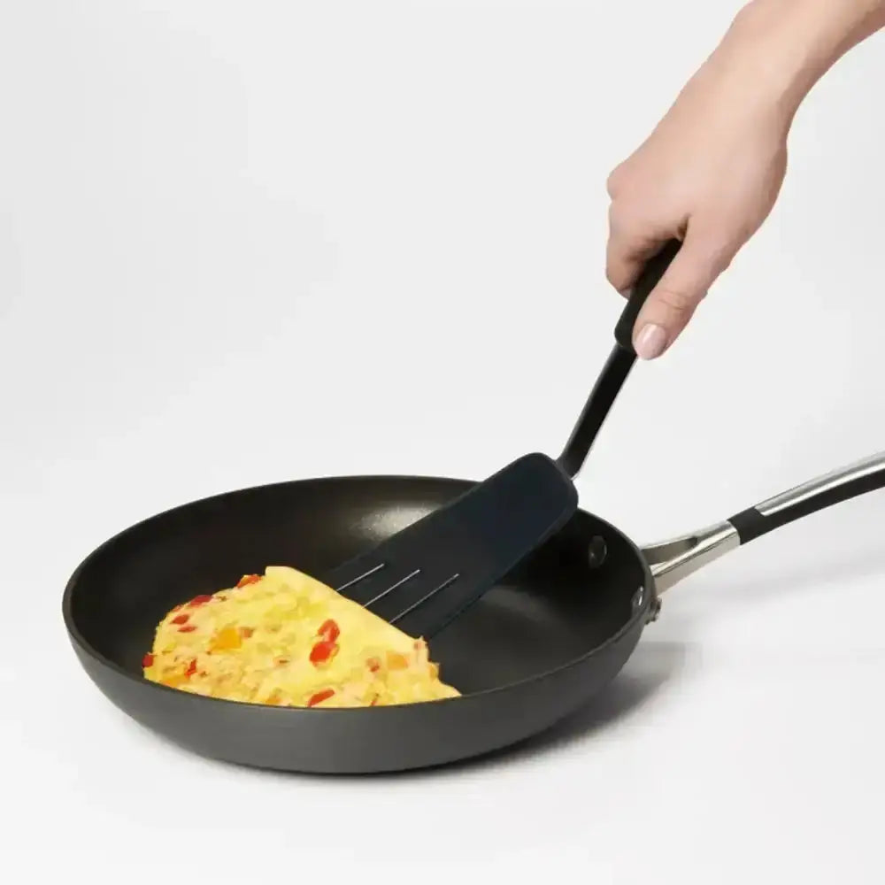 Person flipping an omelette in a frying pan with a spatula on a white background