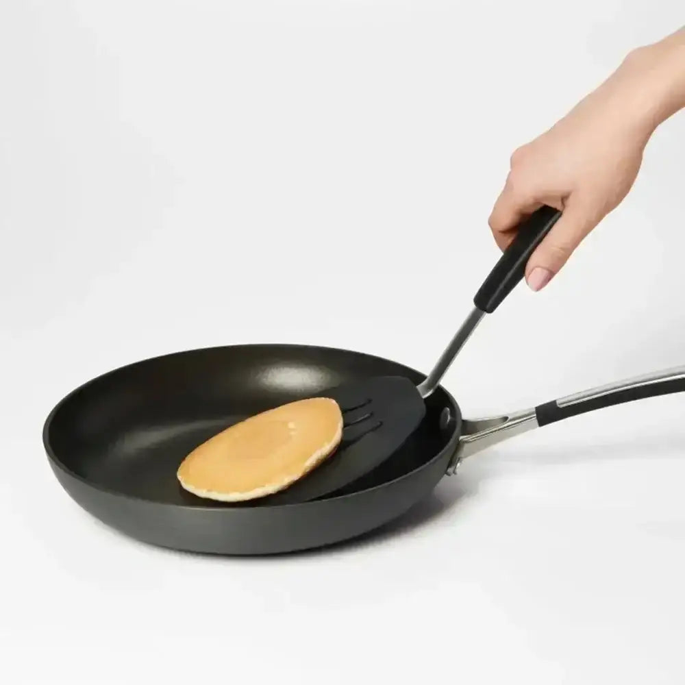 Person flipping a pancake in a black frying pan on a white background