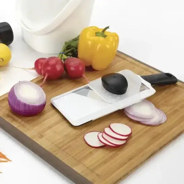 Vegetable peeler on a cutting board with sliced radishes and a yellow bell pepper.