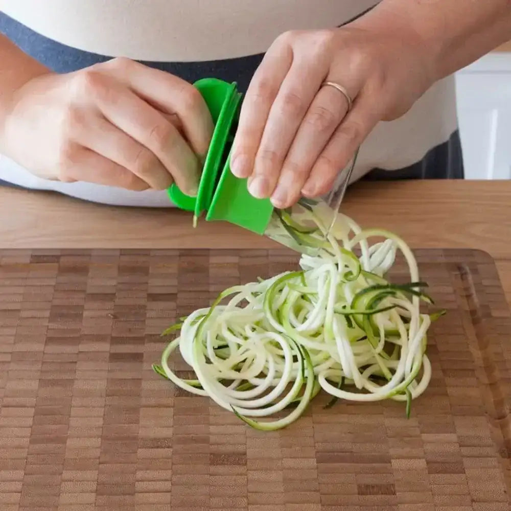 Person using a green spiralizer to make zucchini noodles on a wooden cutting board.