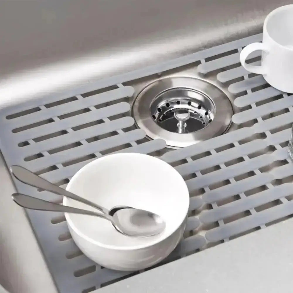 Sinks with a metal drain cover and a white cup on a grid-like mat.