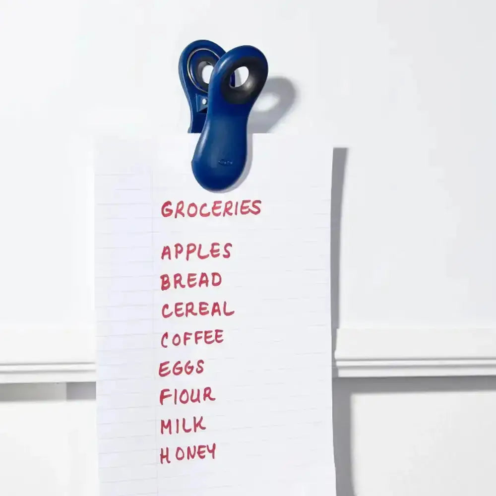White board with grocery list in red marker and a blue clip on a white background