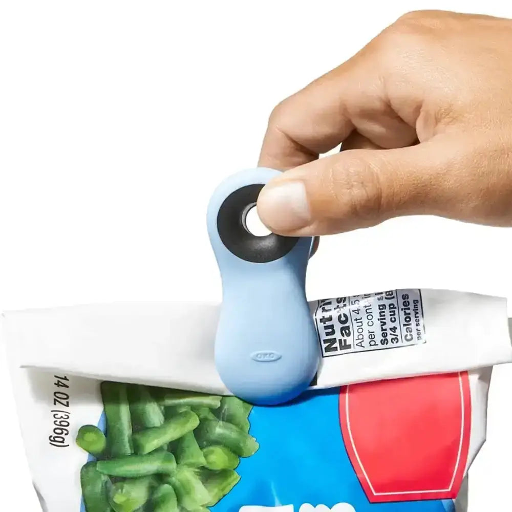 Hand using a blue tool to open a package of green beans with a white background