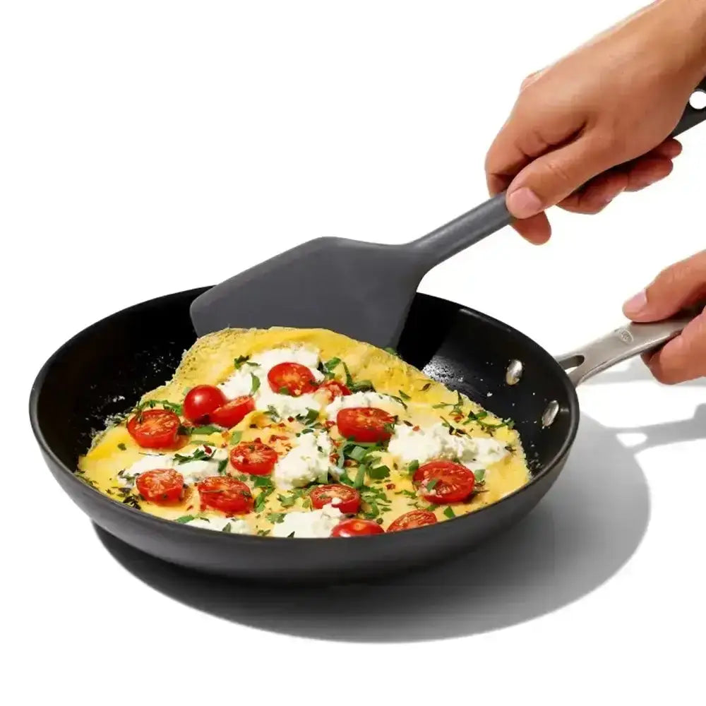 Person using a spatula to serve an omelette with tomatoes and cheese from a frying pan.