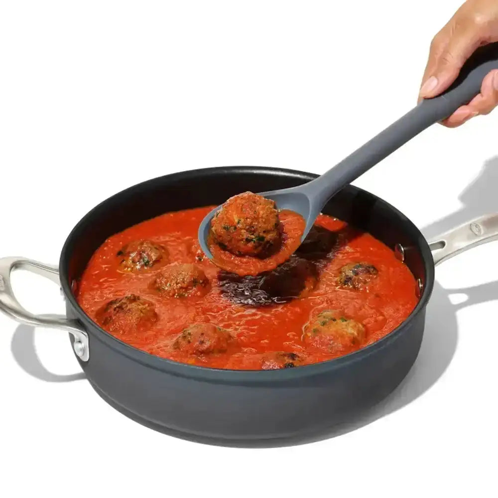 Person ladling meatballs in tomato sauce from a pan with a gray ladle.