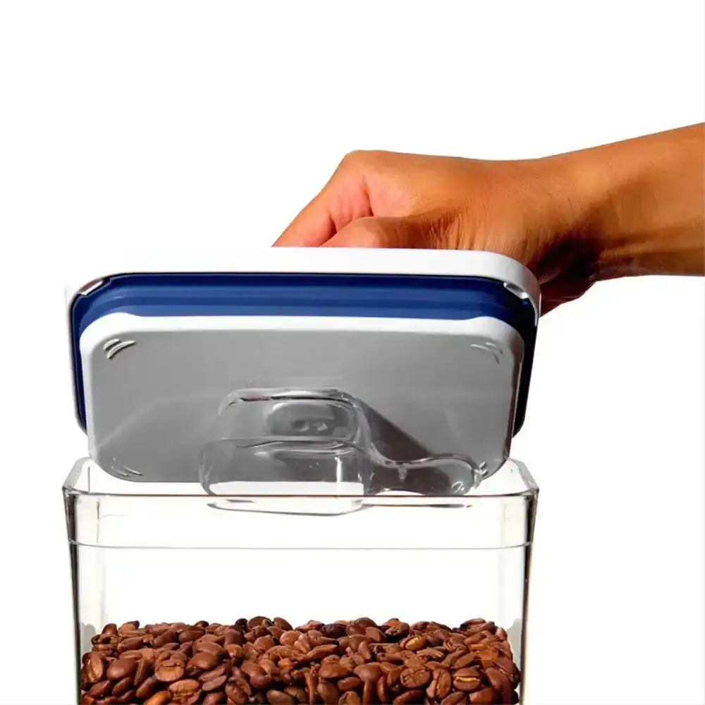 Hand opening a container of coffee beans with a blue lid on a white background
