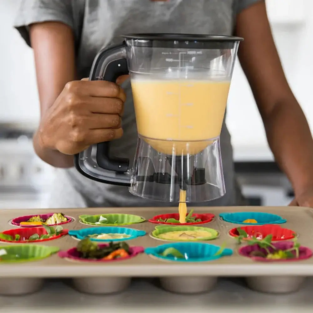Person using a batter dispenser to pour liquid into colorful muffin molds.