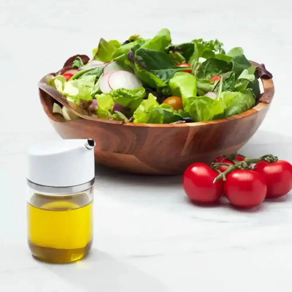 Wooden bowl of salad with a bottle of oil and tomatoes on a white background