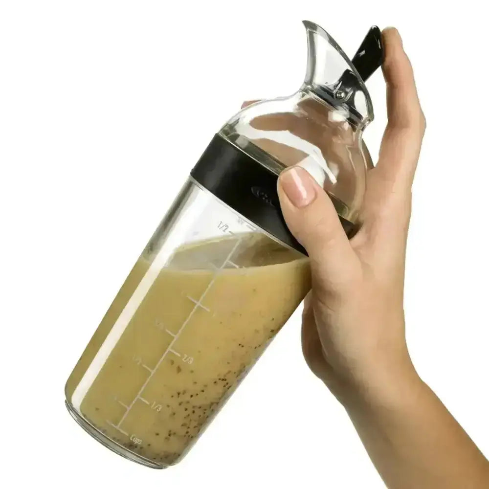Glass measuring cup with handle filled with a brown liquid, held by a hand on a white background