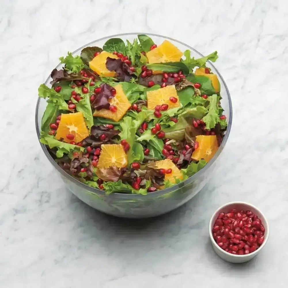 Colorful salad with oranges and pomegranate seeds in a glass bowl on a marble surface.