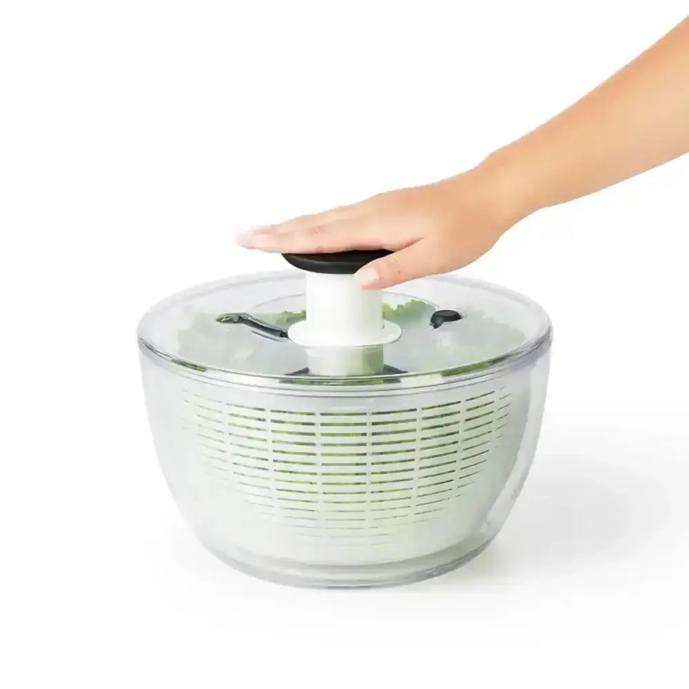 Hand using a salad spinner with lettuce on a white background