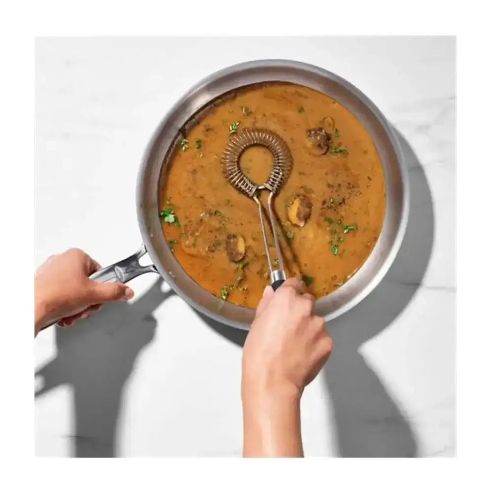 Person holding a frying pan with a creamy dish and a whisk.