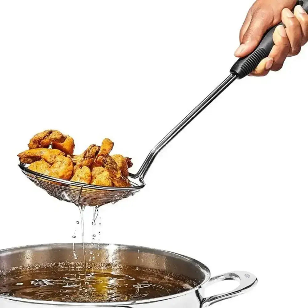 Fried chicken being drained of oil with a skimmer over a frying pan.
