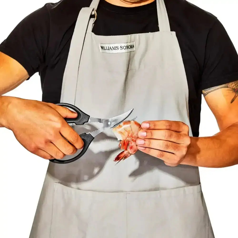 Person in a Williams Sonoma apron using kitchen shears to trim a shrimp.