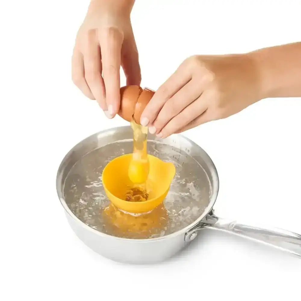 Person cracking an egg into a yellow silicone egg poacher over boiling water.