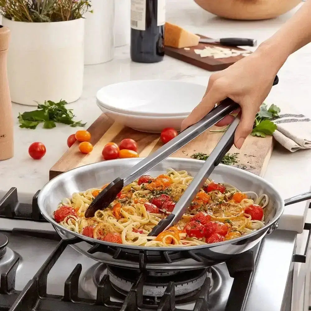 Person cooking pasta with vegetables in a pan on a stove, using tongs.