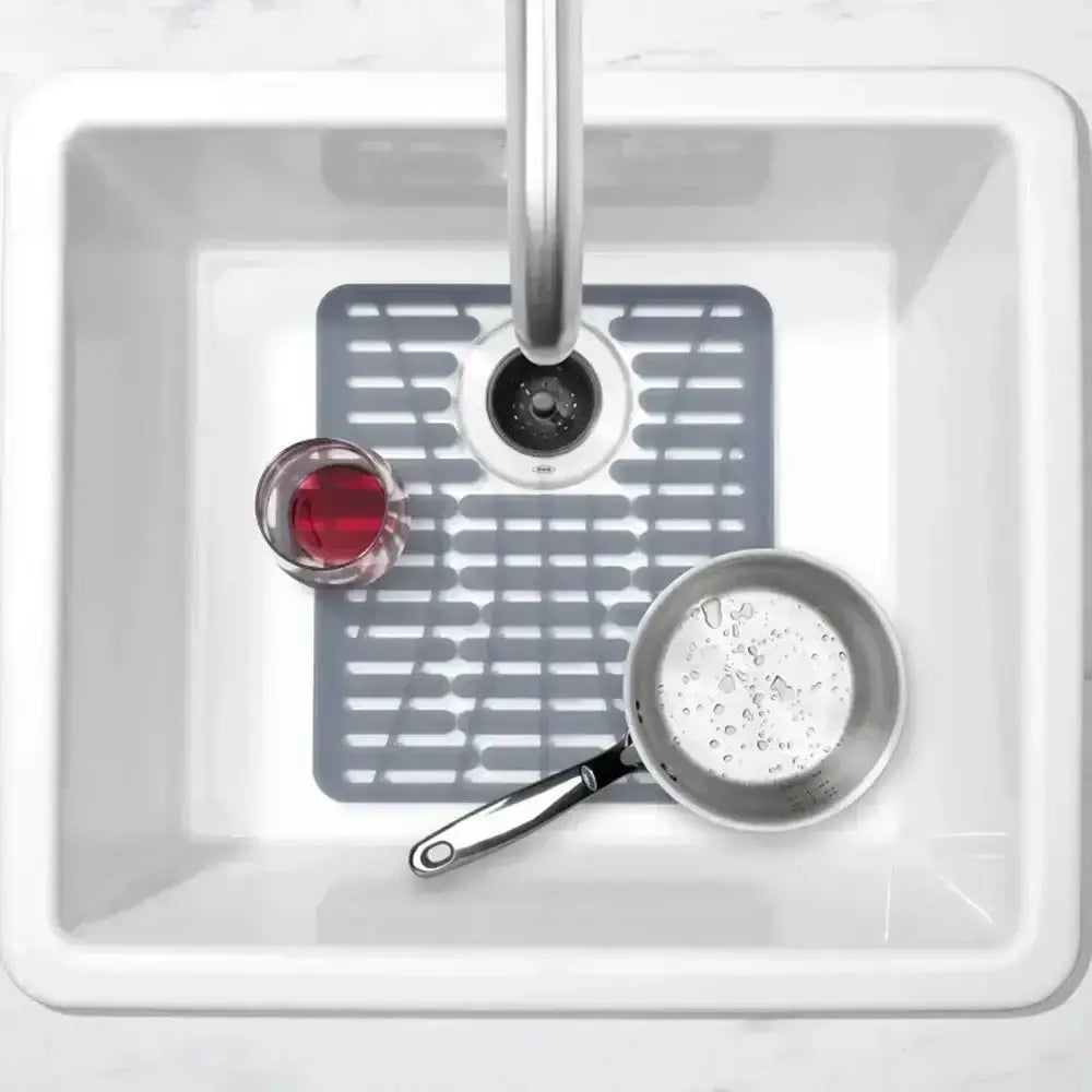 Sink with a gray silicone mat, pan, and small bowl on a white background