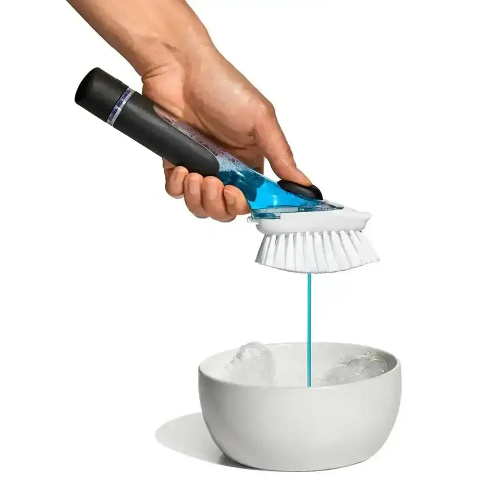 Hand using a cleaning brush with a bottle of cleaning solution on a white bowl.