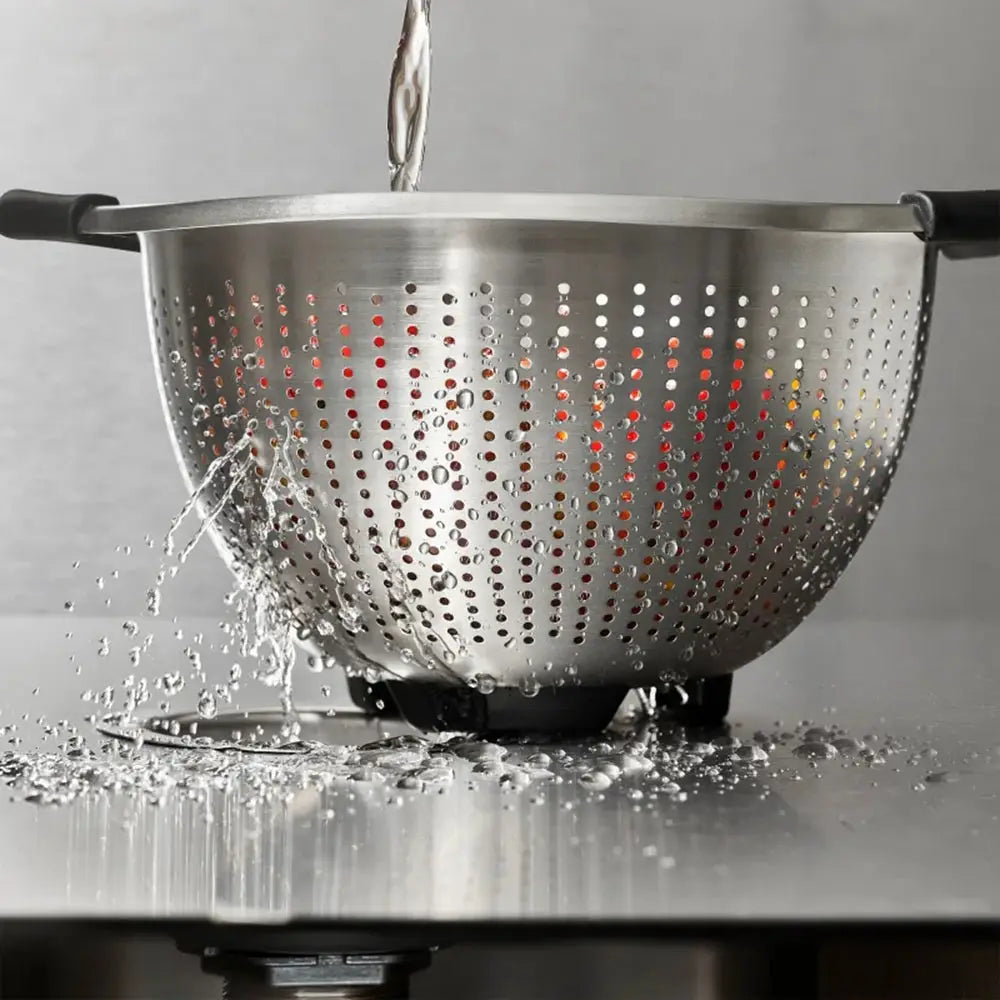 Metal colander being rinsed under running water on a gray background