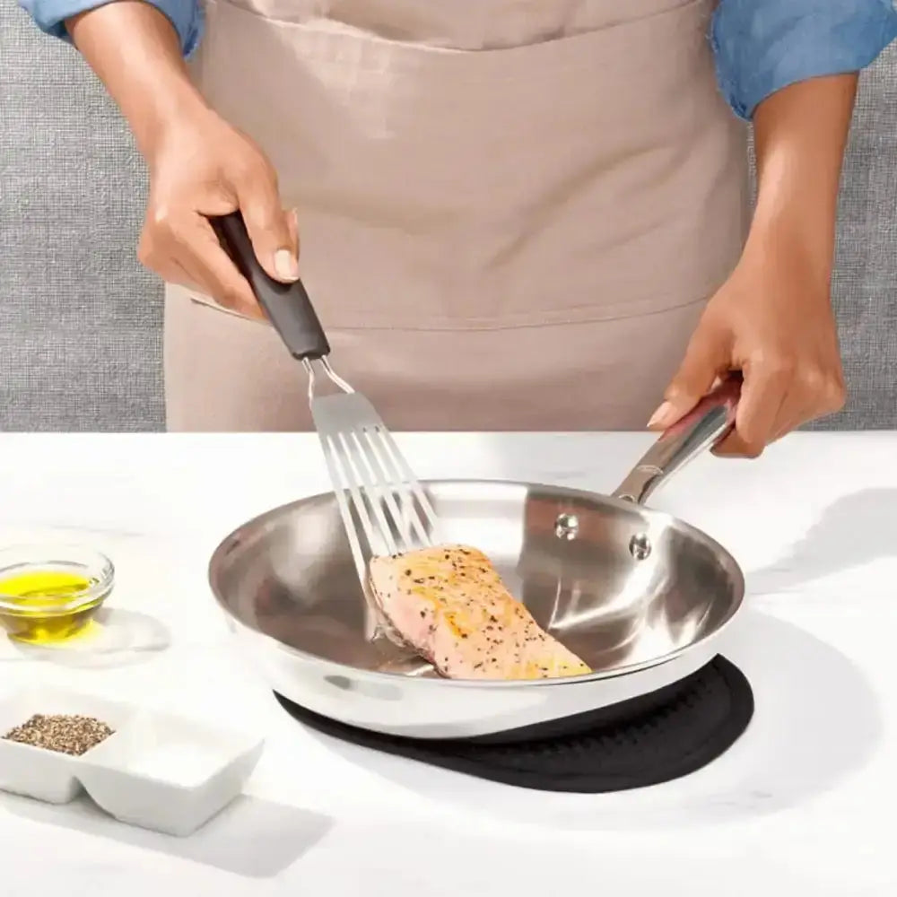 Person cooking salmon in a pan with a spatula, wearing an apron.