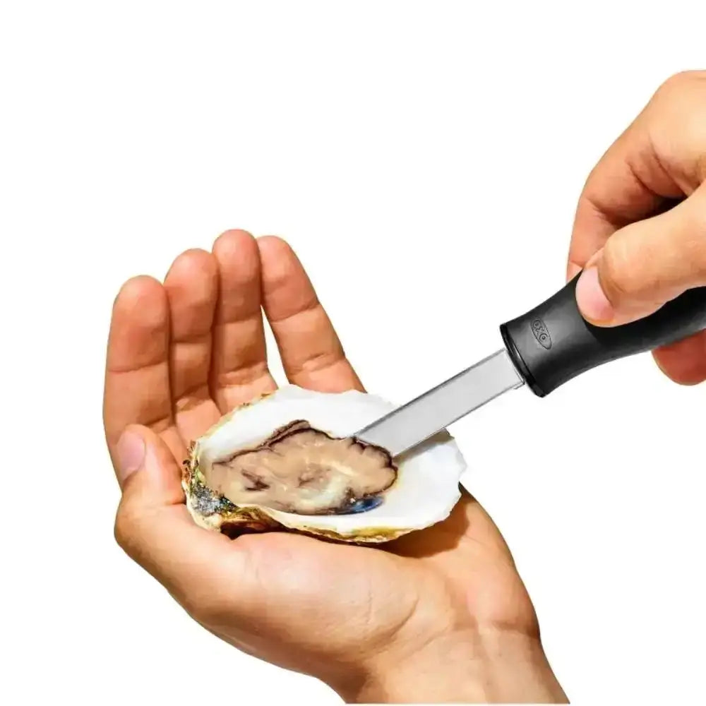 Person opening an oyster with a knife on a white background