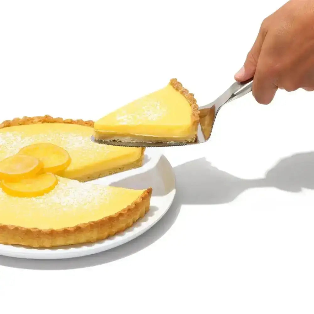 A bright yellow lemon tart slice with golden crust served on an oxo good grips stainless steel pie server and cake lifter