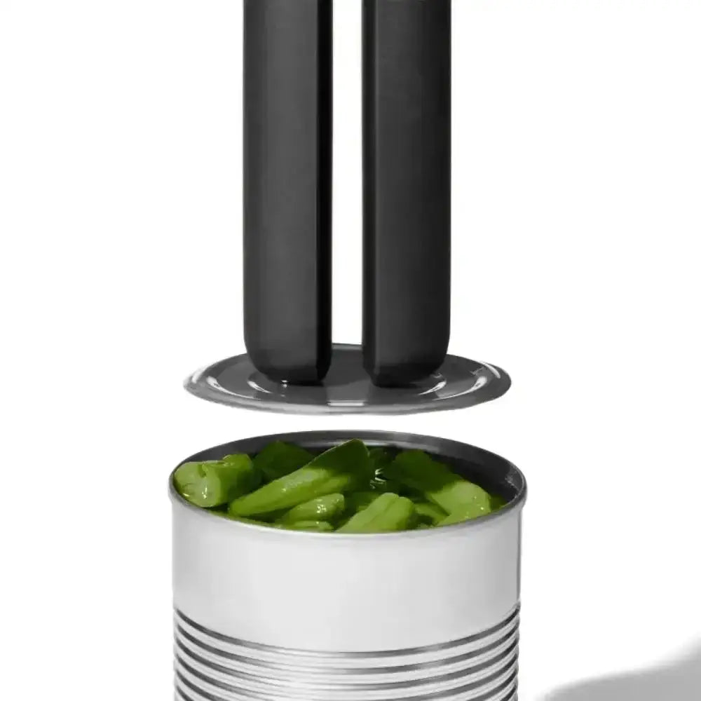 Black can opener lifting the lid off a can of green beans on a white background
