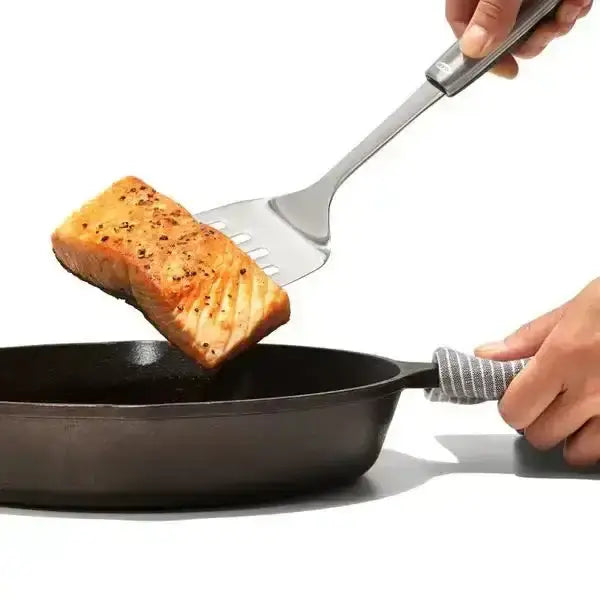 Oxo stainless steel cooking turner lifting golden seared salmon fillet from black cast iron skillet