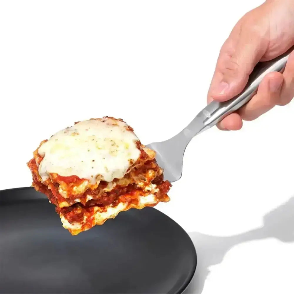Oxo stainless steel lasagna turner lifting a slice of lasagna with melted white cheese and red sauce