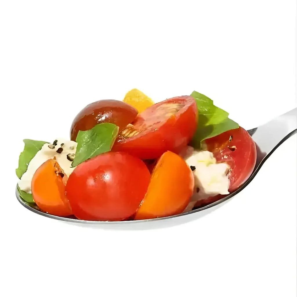 Oxo stainless steel serving spoon holding a shiny silver spoon with cherry tomato salad basil mozzarella and black pepper