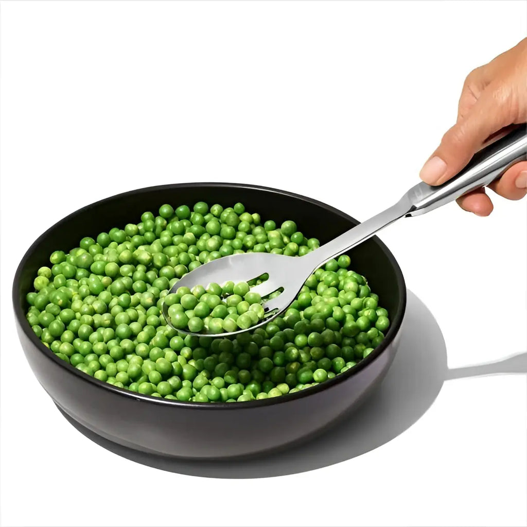 A sleek black bowl with vibrant green peas served using an oxo stainless steel slotted serving spoon