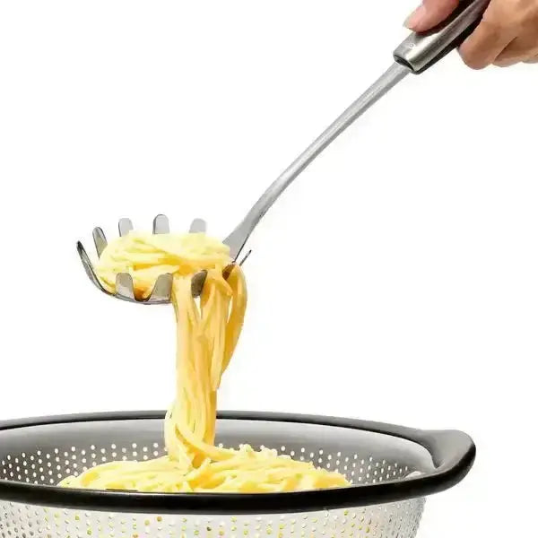 Oxo stainless steel spaghetti server with a polished silver finish and four prongs lifting spaghetti from a black colander